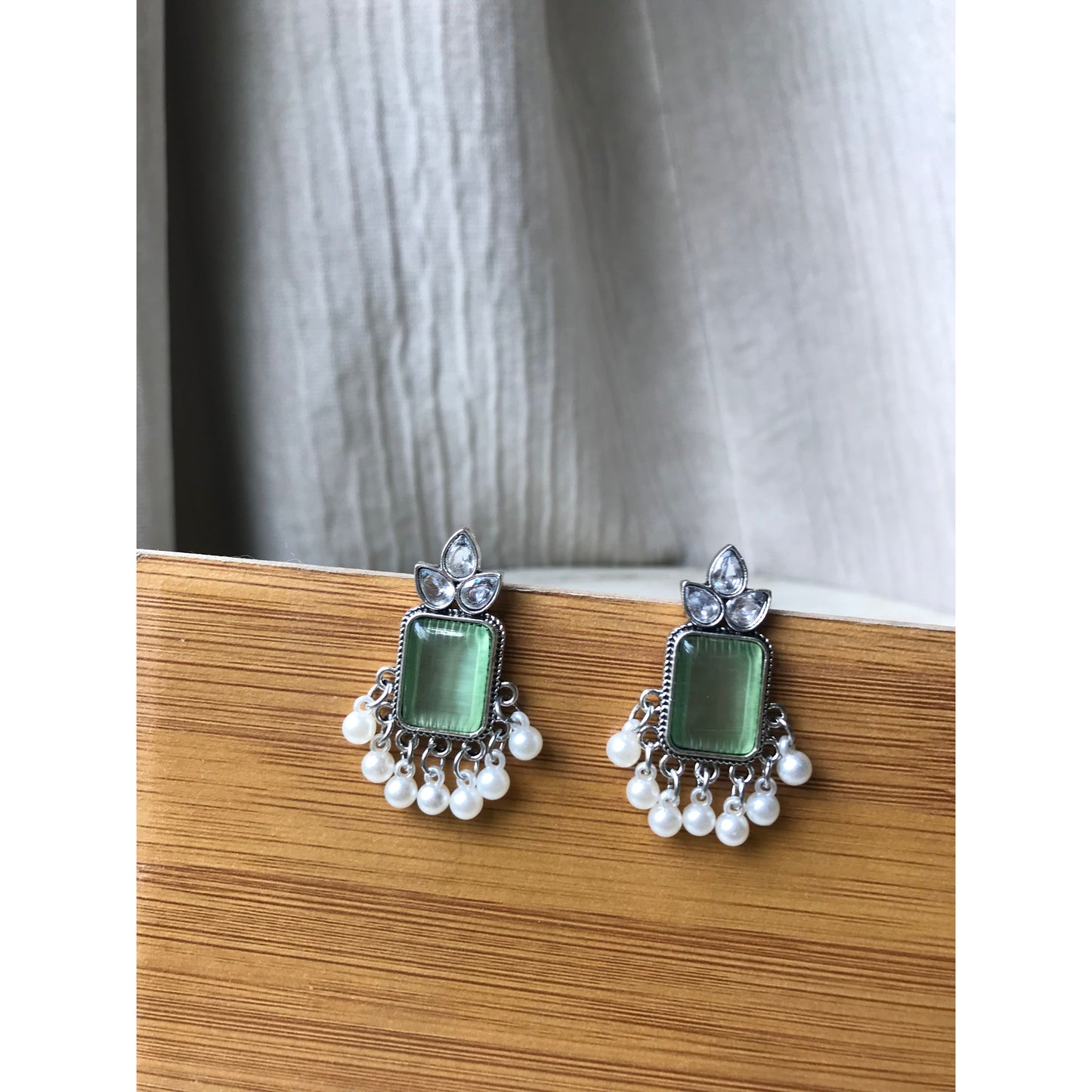 Pair of earrings with green gemstones and pearl accents on a wooden surface.