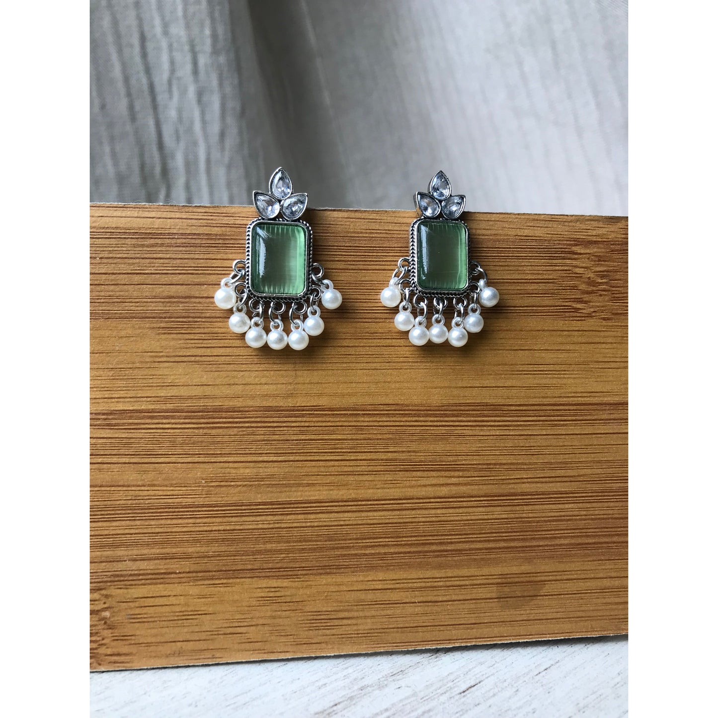 Pair of earrings with green gemstones and silver accents on a wooden surface
