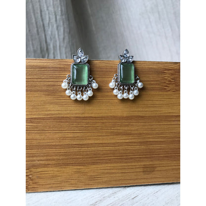 Pair of earrings with green gemstones and silver accents on a wooden surface