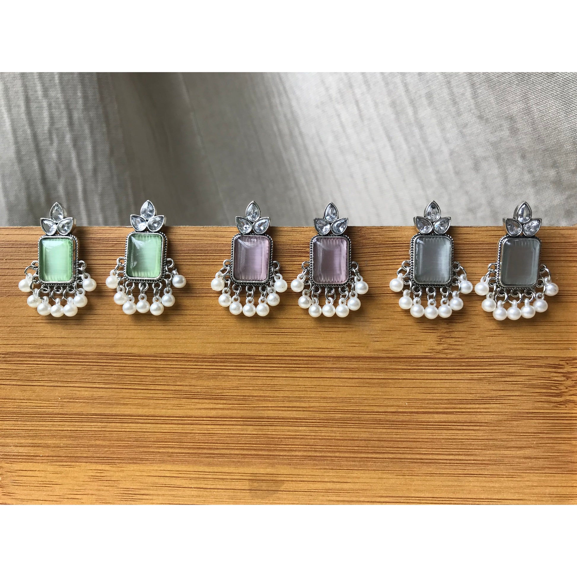 Set of three pairs of earrings with different colored gemstones on a wooden surface.