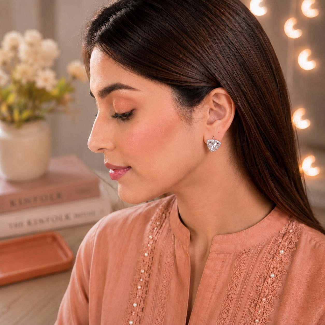 Model wearing triangular silver crystal stud earrings with a round-cut centre stone and pavé halo