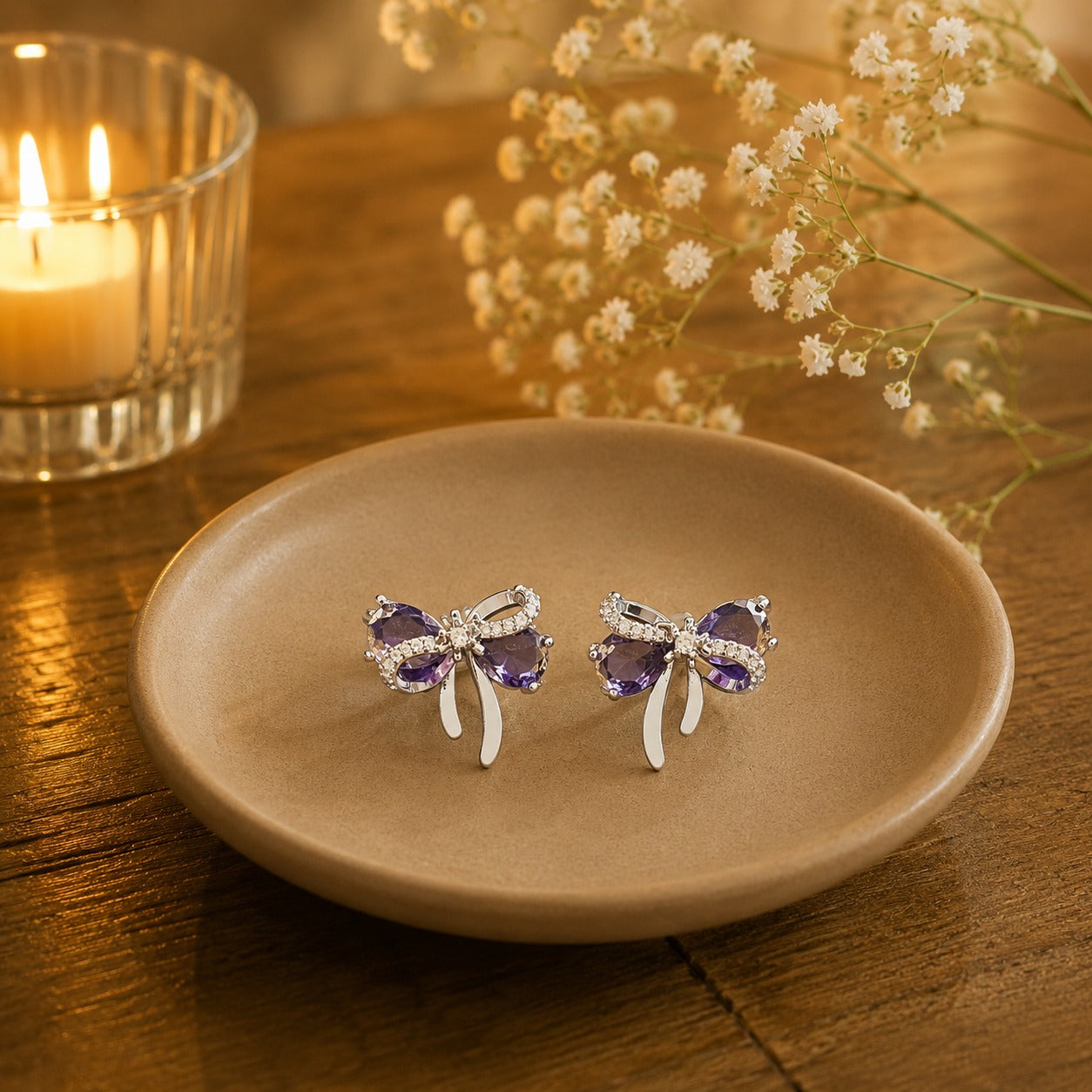Lavender purple bow stud earrings on beige ceramic plate.