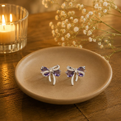 Lavender purple bow stud earrings on beige ceramic plate.