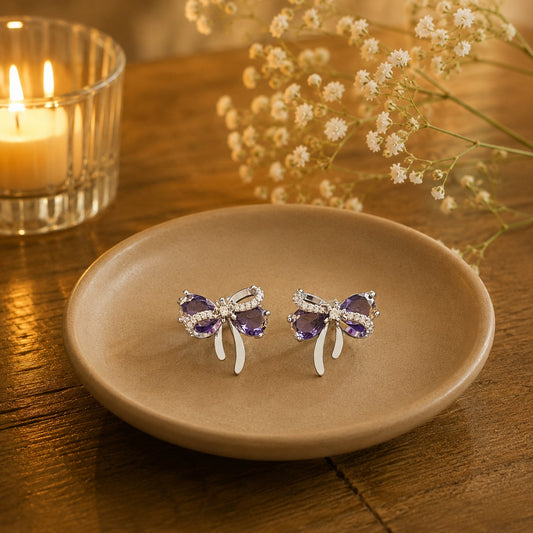 Lavender purple bow stud earrings on beige ceramic plate.