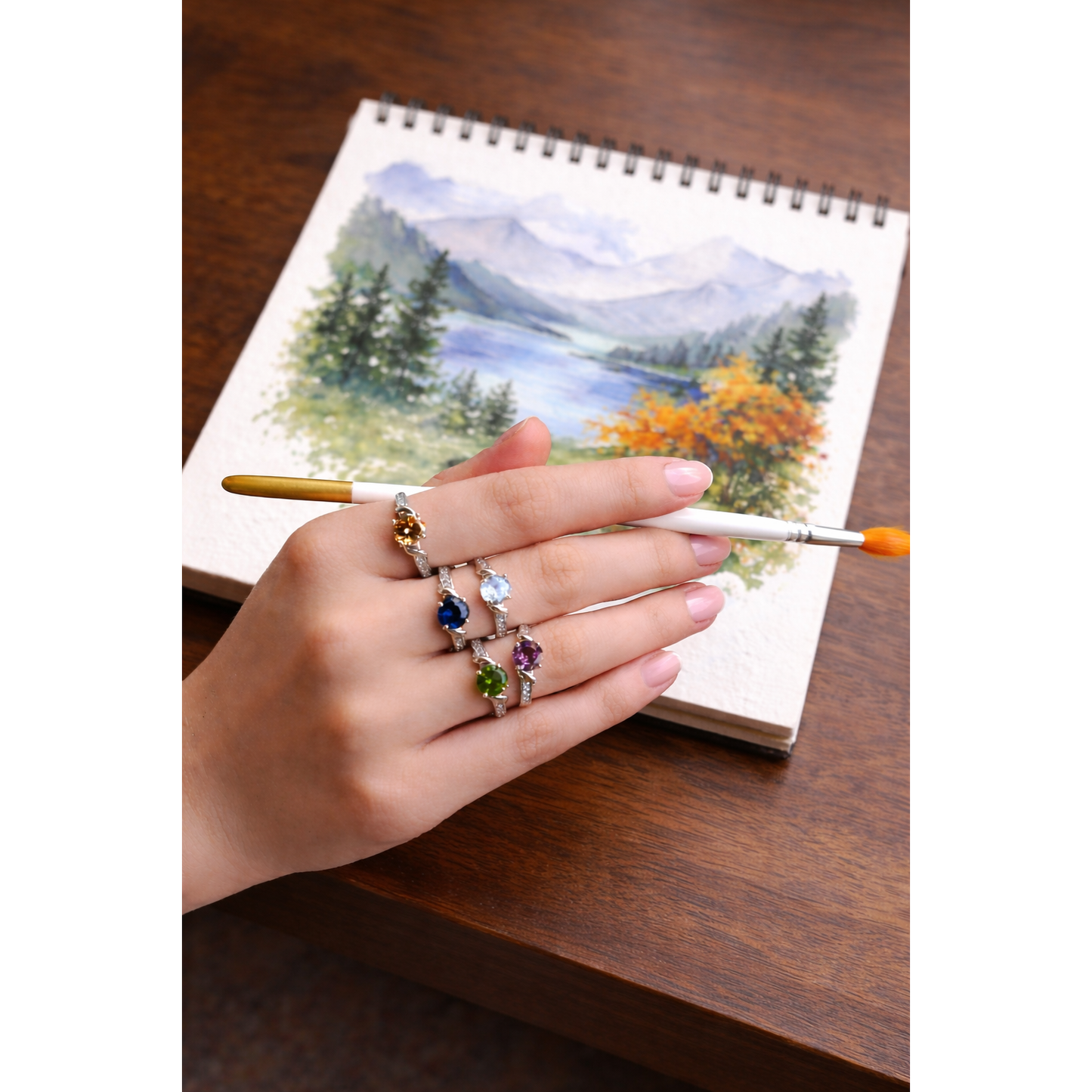 Woman wearing multi-colour twist solitaire silver ring collection while holding paintbrush over sketchbook painting