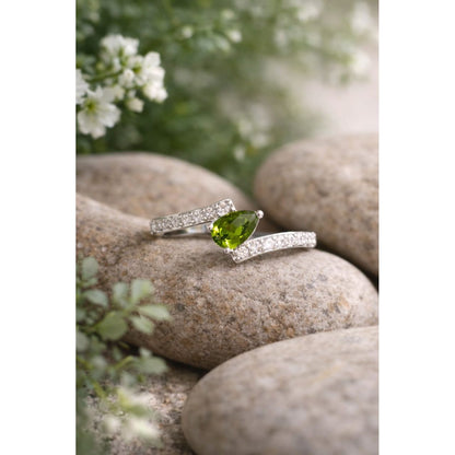Silver ring with an olive green gemstone on a stone surface with blurred flowers in the background