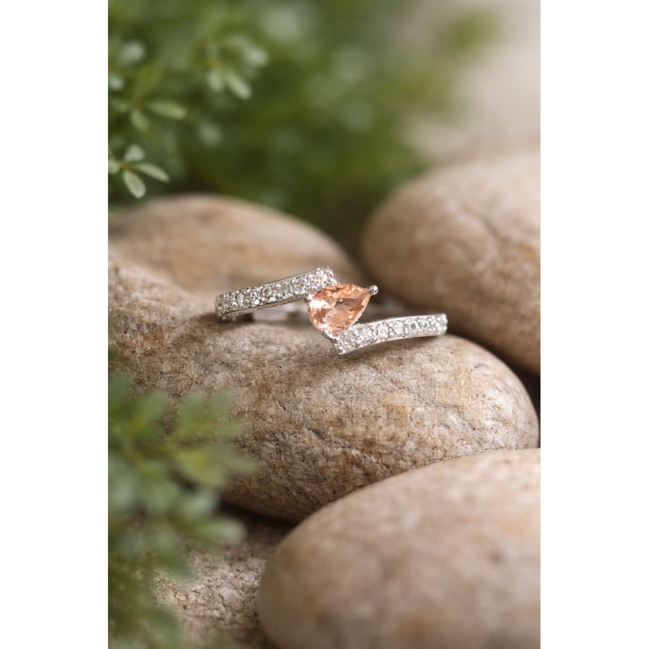 Silver ring with a  champaign gemstone on a stone surface with blurred flowers in the background