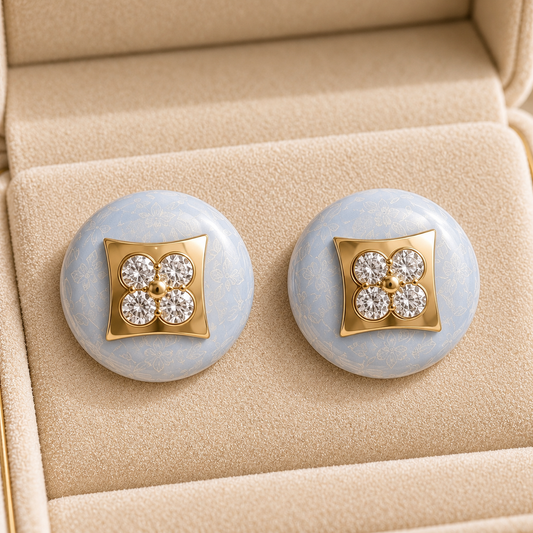 Powder Crest Stud Earrings displayed in a jewellery box with pale blue round bases, geometric gold-tone centres and clear zircon accents.