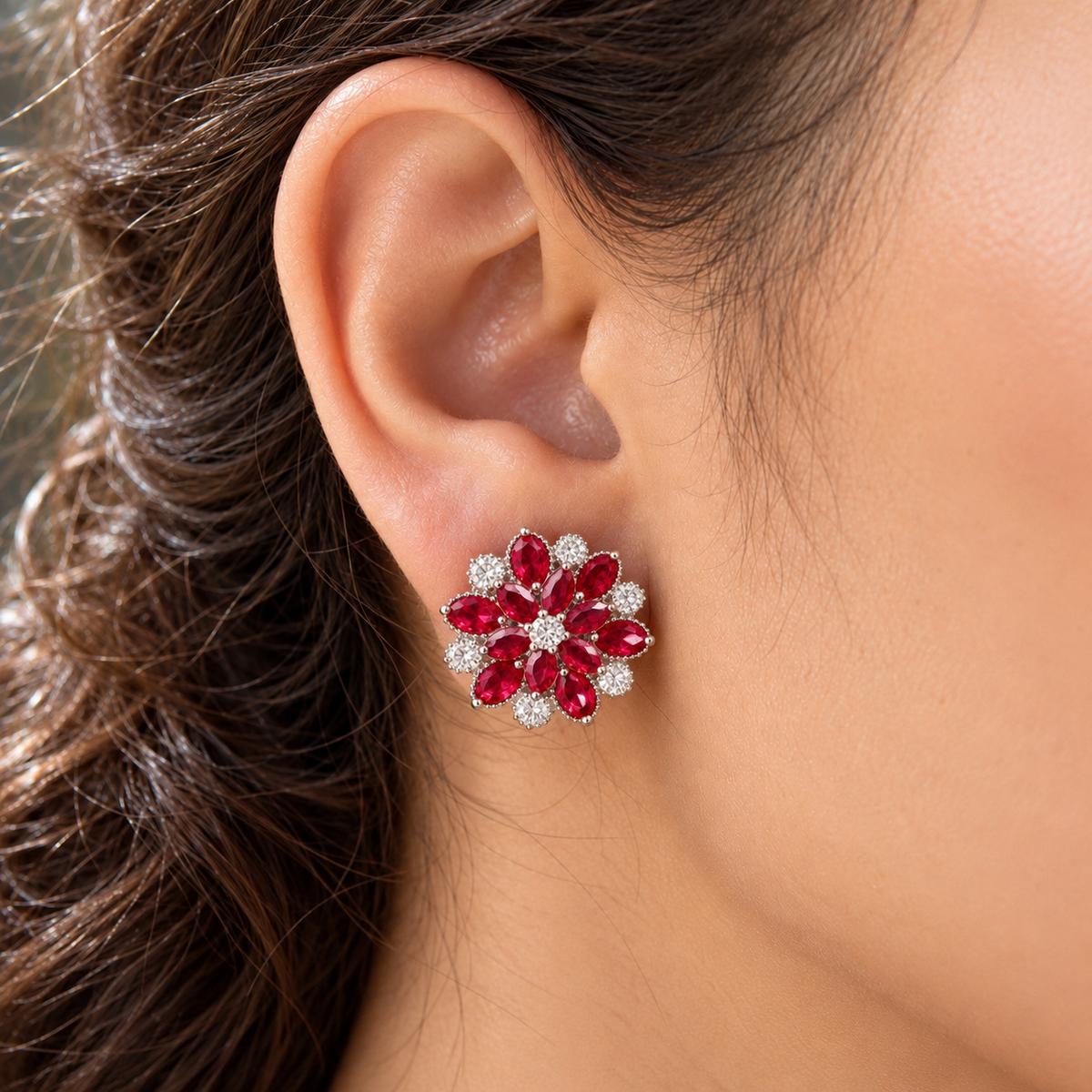 Close-up of a woman's ear wearing the Vespera Bloom ruby red floral stud earring, featuring vivid red gemstone petals and brilliant clear zircon detailing.