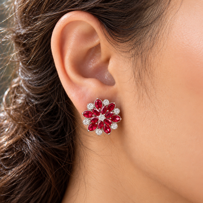Close-up of a woman's ear wearing the Vespera Bloom ruby red floral stud earring, featuring vivid red gemstone petals and brilliant clear zircon detailing.