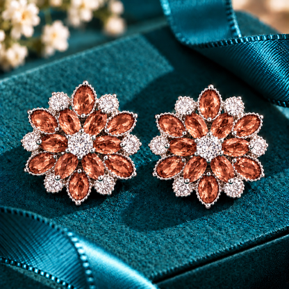 Vespera Bloom Earrings in muted rust, featuring layered marquise-cut gemstones, clear zircon accents and polished silver-tone settings, displayed on a teal jewellery box