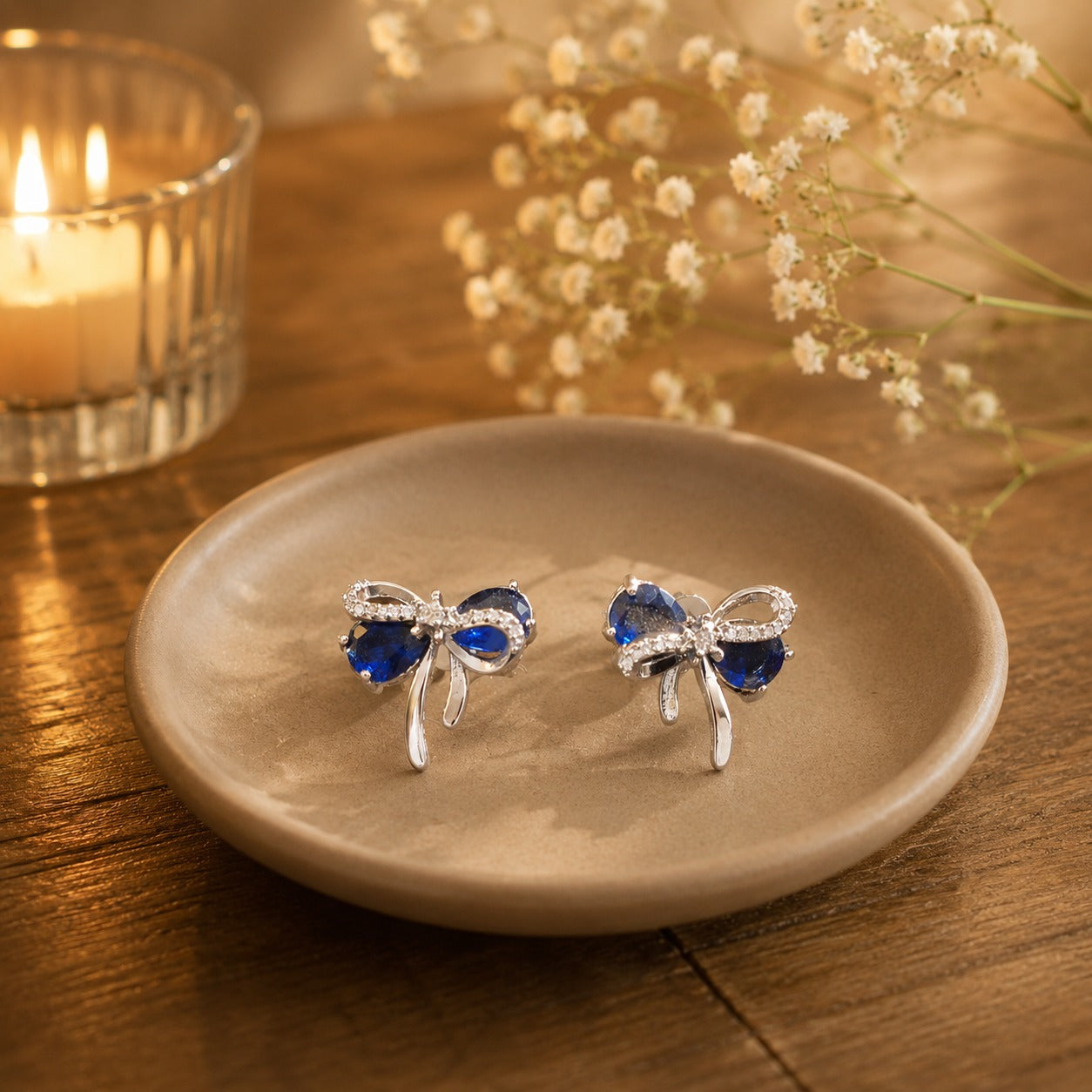 Sapphire blue bow stud earrings on beige ceramic plate.