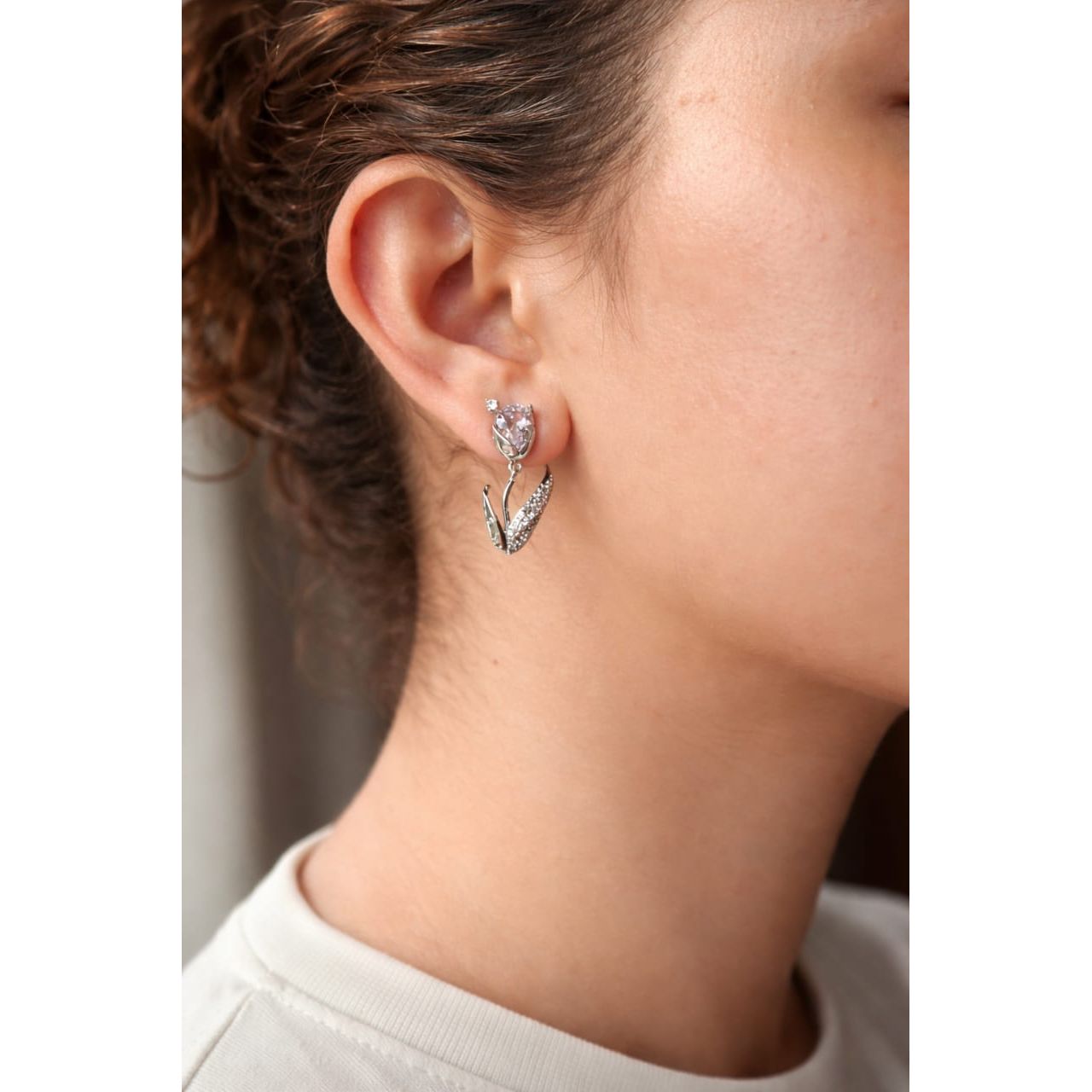 Close-up of a silver tulip-shaped drop earring with a  soft lavender crystal ,faceted gemstone and pavé leaf detail worn on a woman’s ear