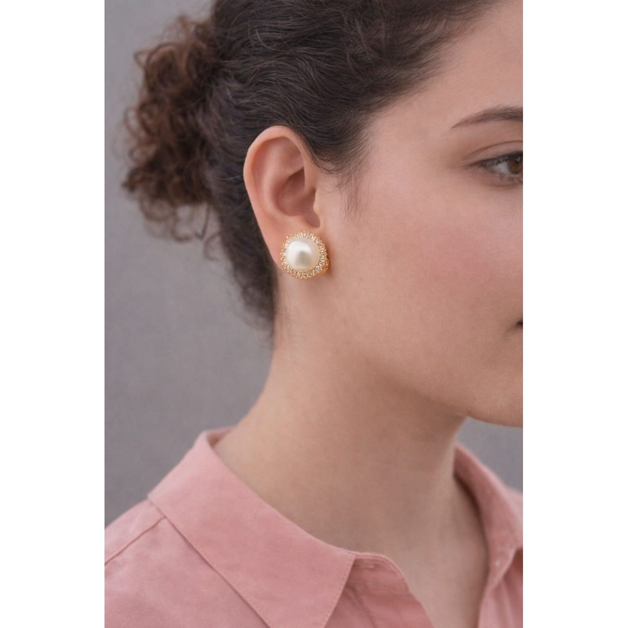 Woman wearing gold pearl halo clip on stud earrings with crystal border shown in side profile under soft lighting