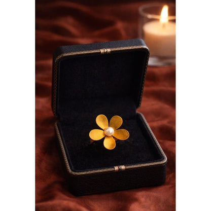 Gold flower pearl statement ring displayed inside dark velvet jewelry box with blurred candle background