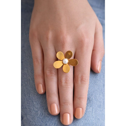 Gold floral statement ring with pearl center worn on feminine hand over light denim background