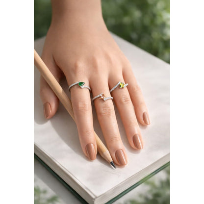 Hand wearing three silver rings with gems with a pencil on a white surface