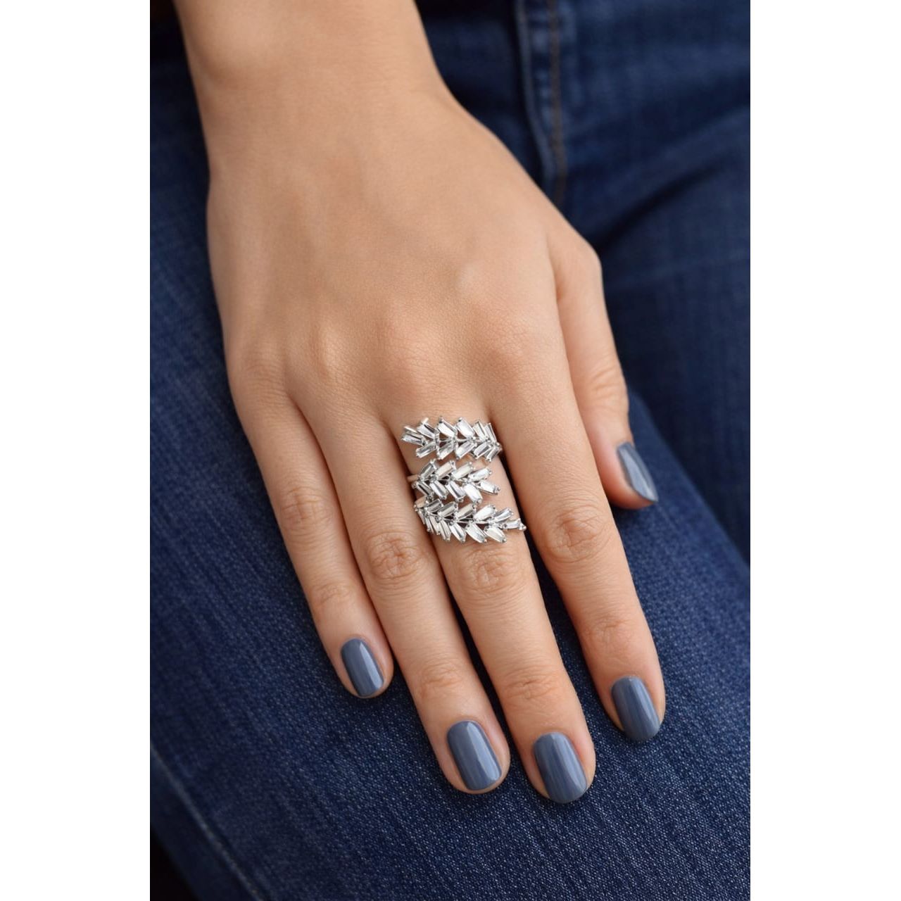 Silver crystal cluster statement ring worn on hand with grey nail polish, showcasing layered baguette stones and modern wrap design