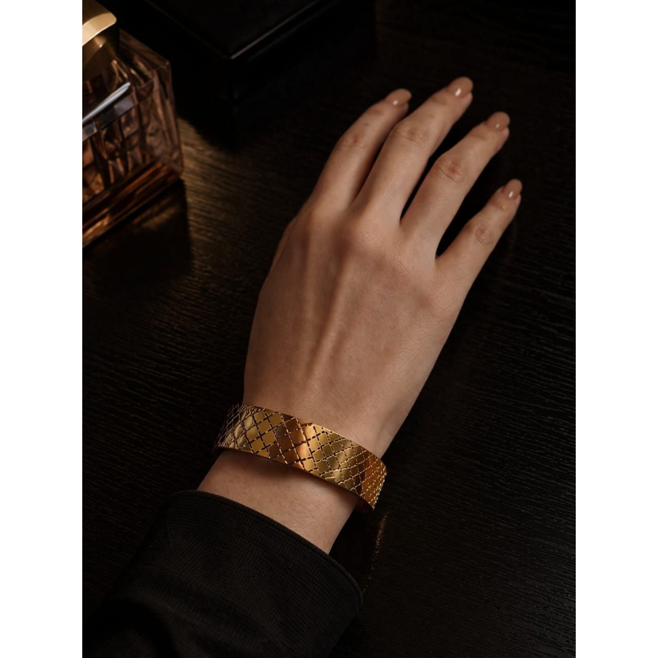 Gold textured cuff bracelet with cross pattern worn on wrist on dark wooden table setting