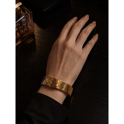 Gold textured cuff bracelet with cross pattern worn on wrist on dark wooden table setting
