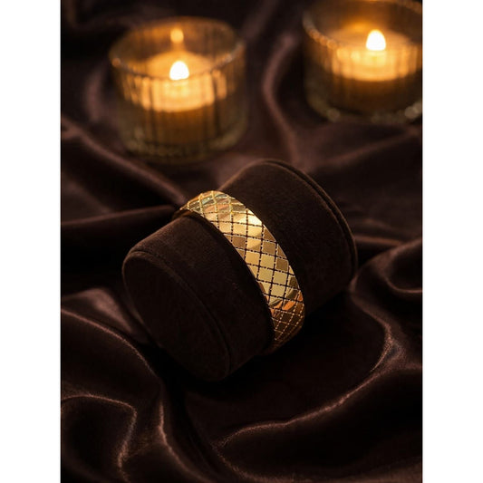 Gold textured cuff bracelet with cross pattern displayed on velvet stand with warm candlelight background