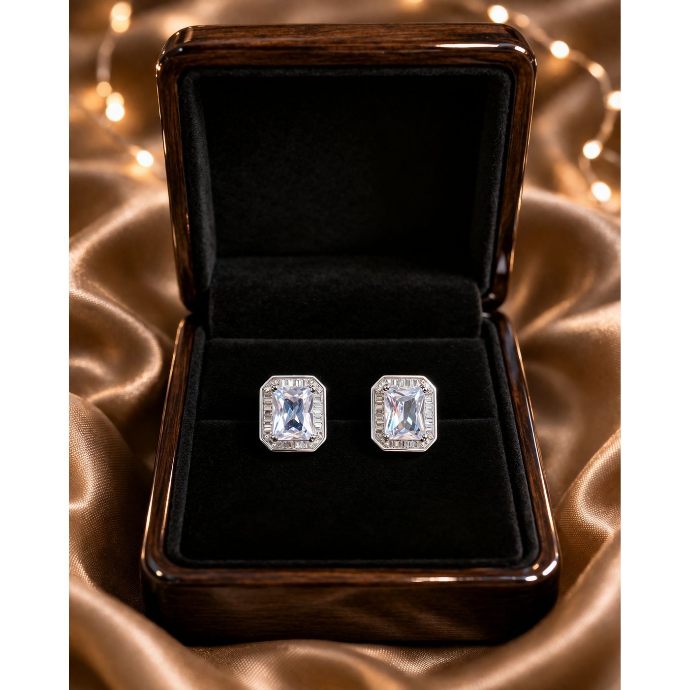 Silver emerald-cut crystal stud earrings displayed in premium jewelry box on satin fabric with warm lights