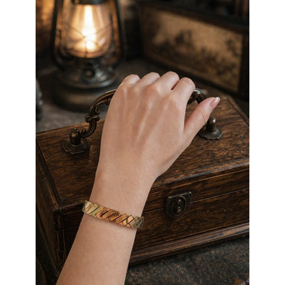 Gold woven cuff bracelet with lock worn on wrist over vintage wooden chest with warm lantern lighting
