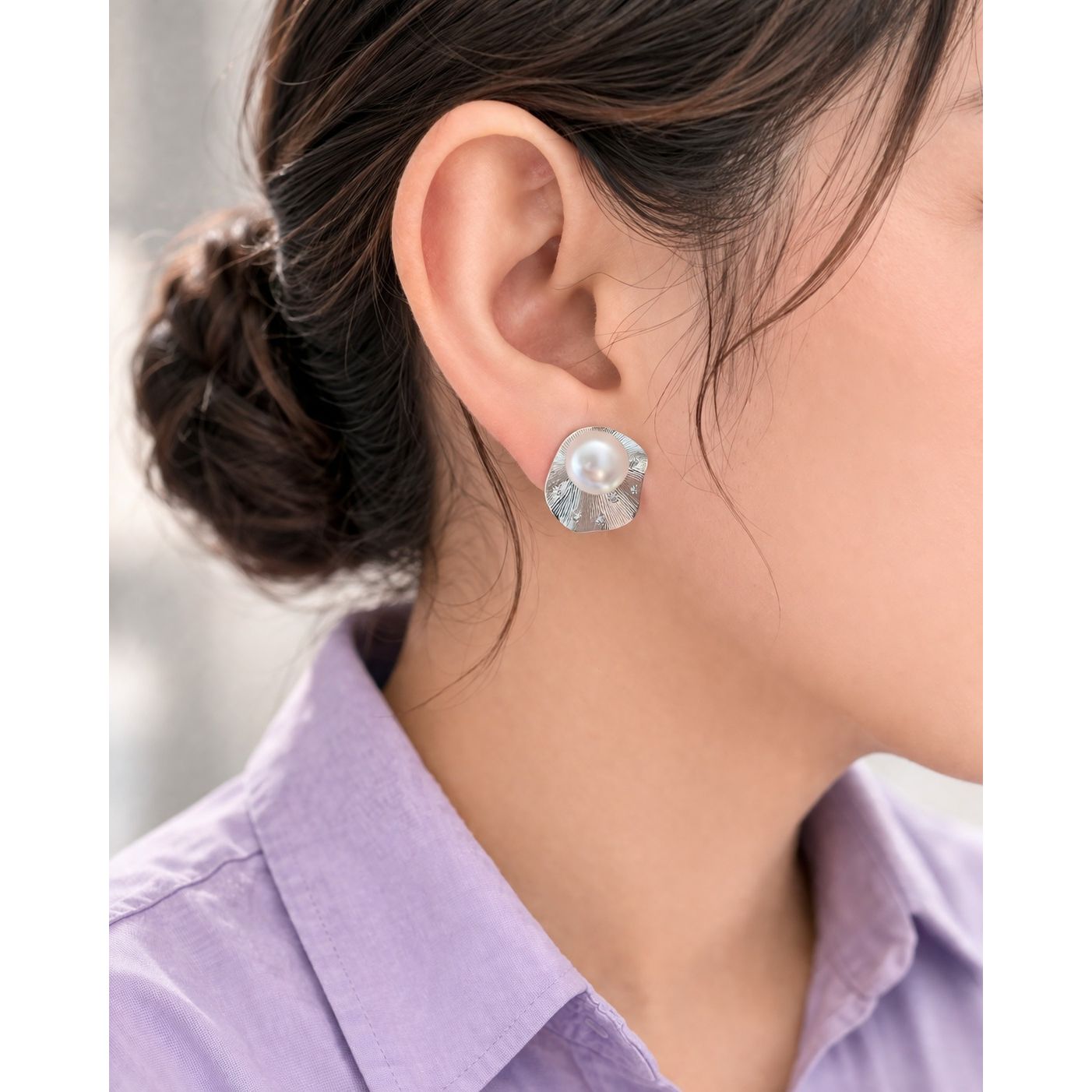 Side profile model wearing silver textured pearl stud earrings with  radiant metal design 
