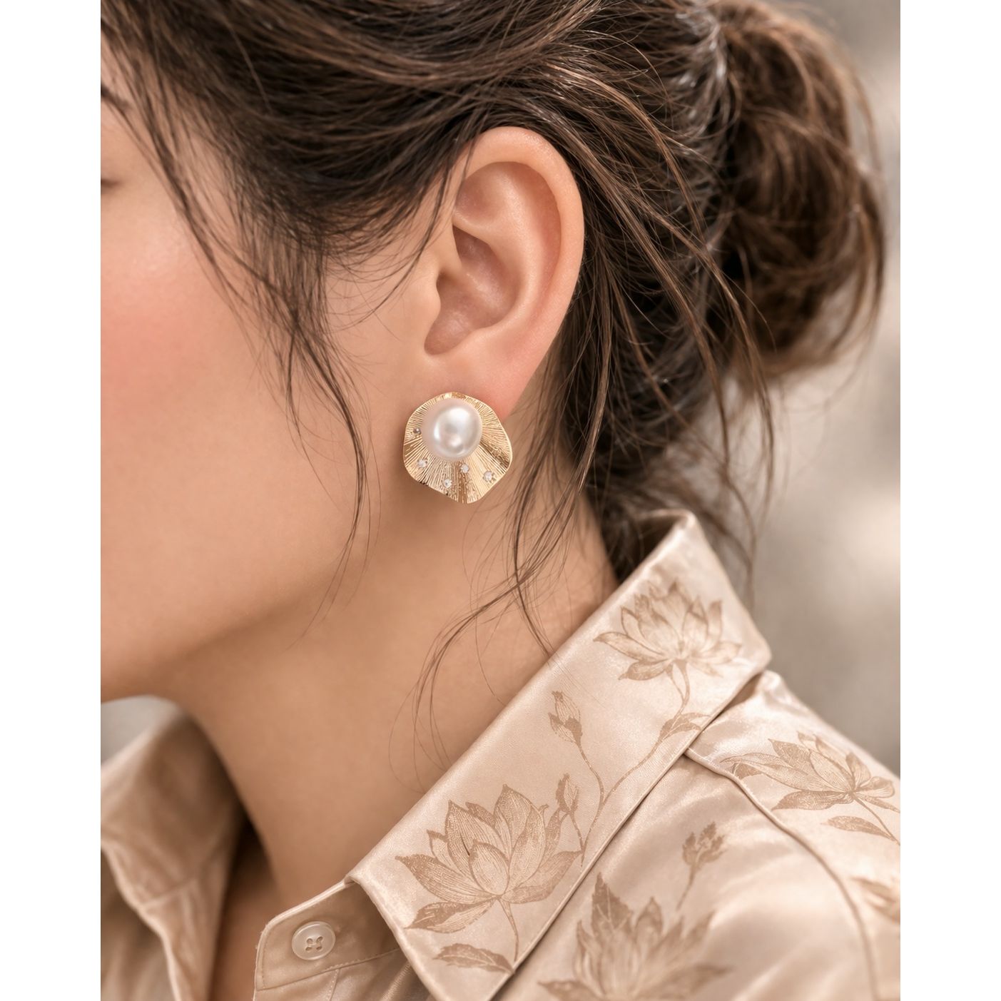Side profile model wearing gold textured pearl stud earrings with radiant metal design 