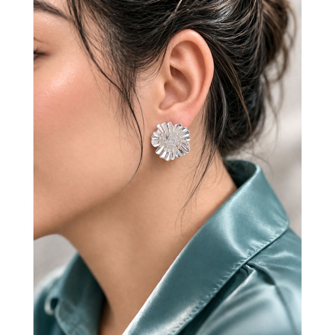 Side profile model wearing silver floral stud earrings with textured petal design 