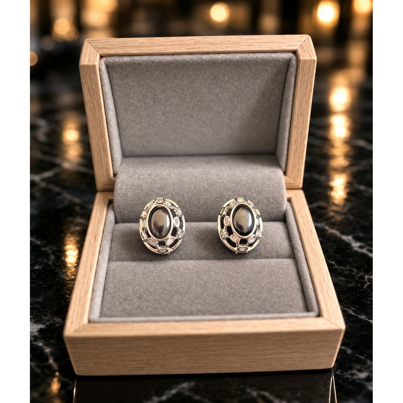 Silver oval black stone earrings placed in grey velvet jewelry box with warm ambient background lighting