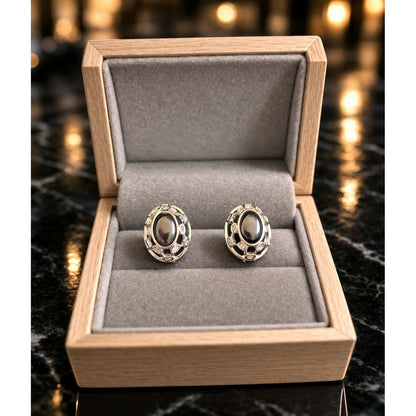 Silver oval black stone earrings placed in grey velvet jewelry box with warm ambient background lighting