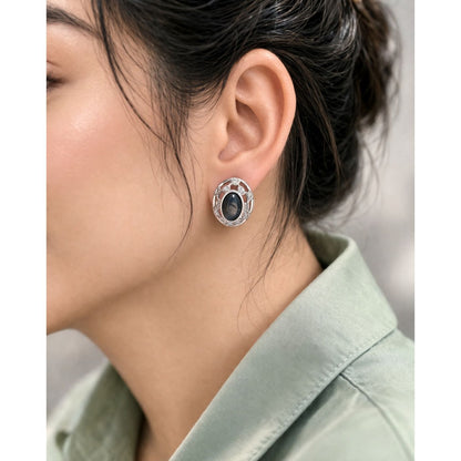 Silver oval black stone stud earrings worn on ear with soft natural lighting and minimal styling