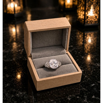 Silver solitaire ring with pavé band displayed in light wood jewelry box with velvet interior on marble surface