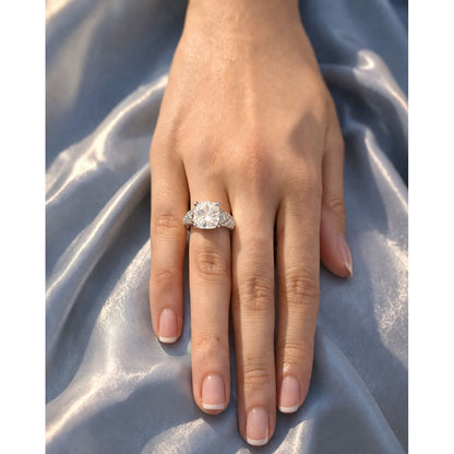 Silver solitaire statement ring with large round stone worn on hand with soft blue satin background
