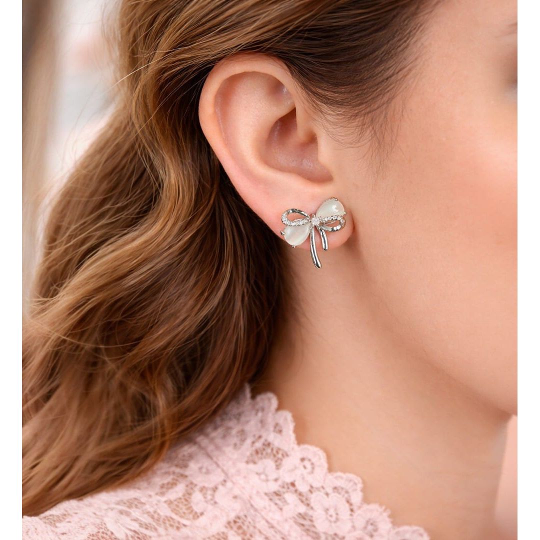 Silver bow knot stud earrings with frosted petals worn on ear close-up