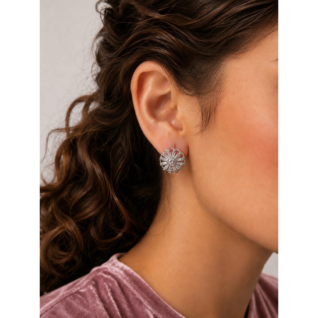 Silver sunburst stud earrings worn on ear with pink outfit close-up