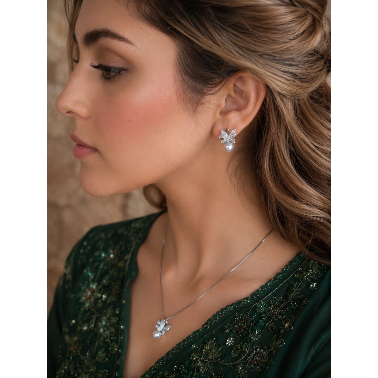 Woman wearing silver butterfly pearl earrings and matching pendant necklace with emerald green embroidered outfit in soft luxury portrait styling