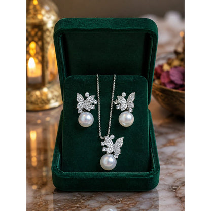 Silver butterfly pearl necklace set with matching earrings displayed inside deep emerald velvet jewelry box on reflective marble surface