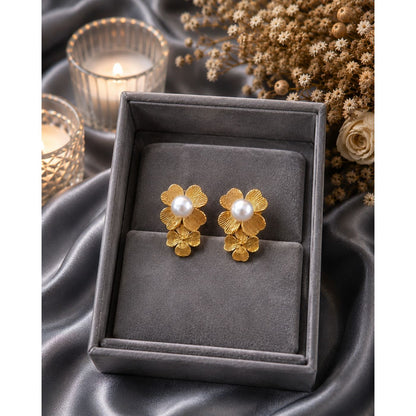 Gold flower pearl stud earrings displayed in a premium charcoal grey jewelry box on satin fabric with candlelit luxury background.