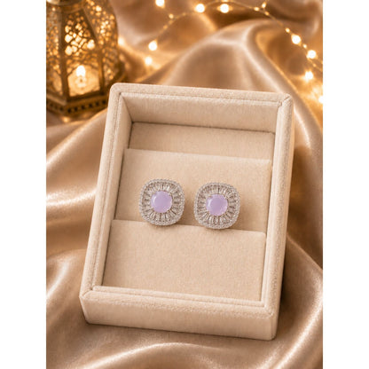 Silver halo stud earrings featuring soft blush pink center stones displayed in a premium ivory jewelry box on champagne satin with warm ambient lighting.
