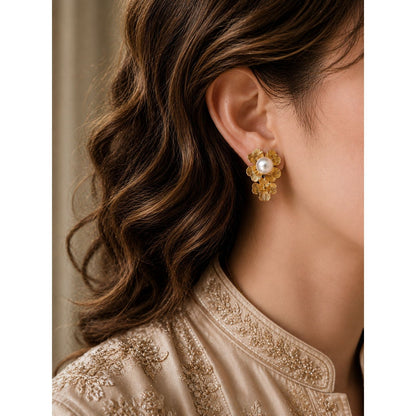 Woman wearing gold floral pearl stud earrings with champagne beige embroidered outfit and soft curled hair in luxury side-profile portrait.