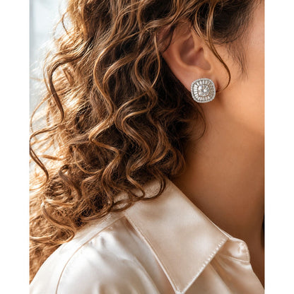 Woman wearing silver crystal halo stud earrings with brilliant white center stone and baguette crystal detailing, styled with a white satin shirt and soft curls.