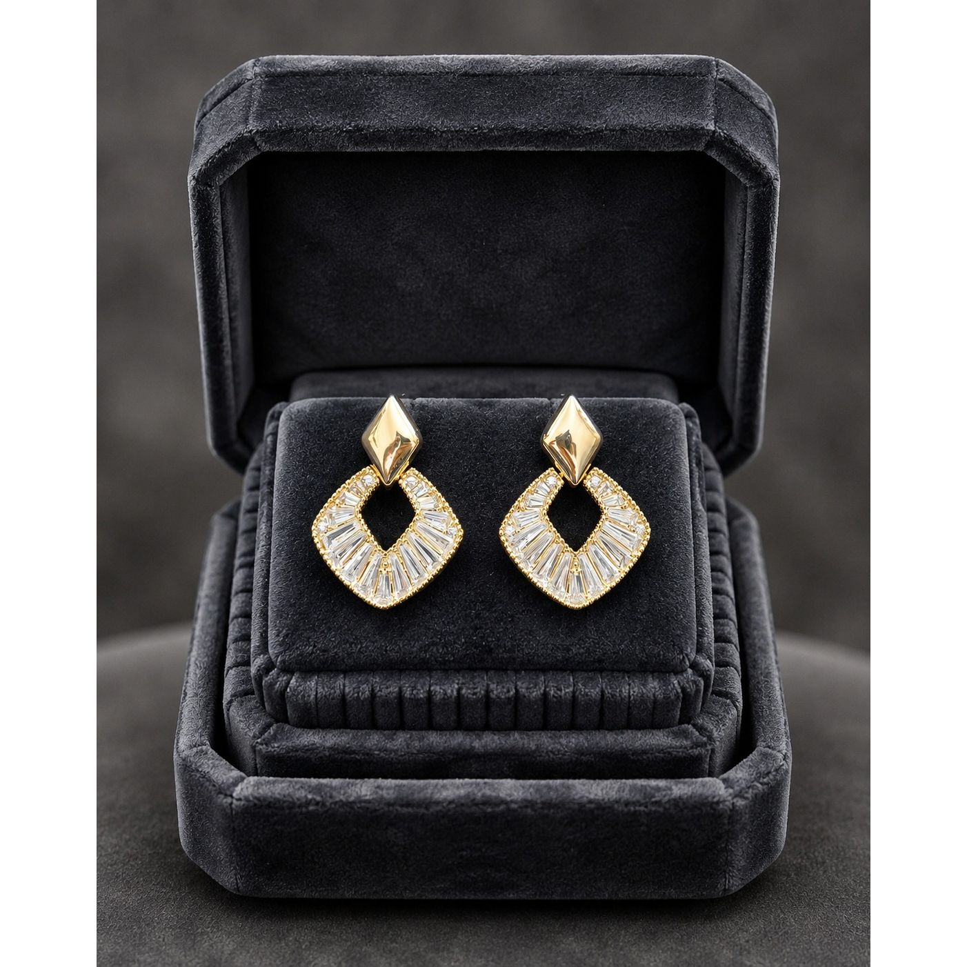 Gold geometric crystal earrings displayed in a premium charcoal velvet jewelry box with luxury studio lighting.