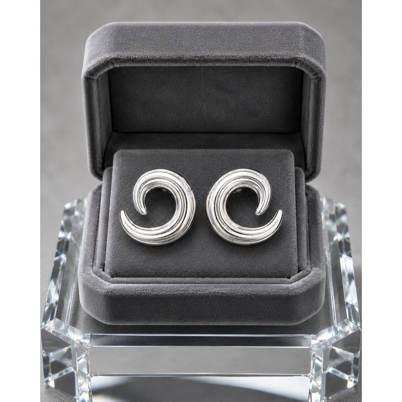 Silver spiral stud earrings displayed in a premium charcoal velvet jewelry box with contemporary sculptural swirl detailing.