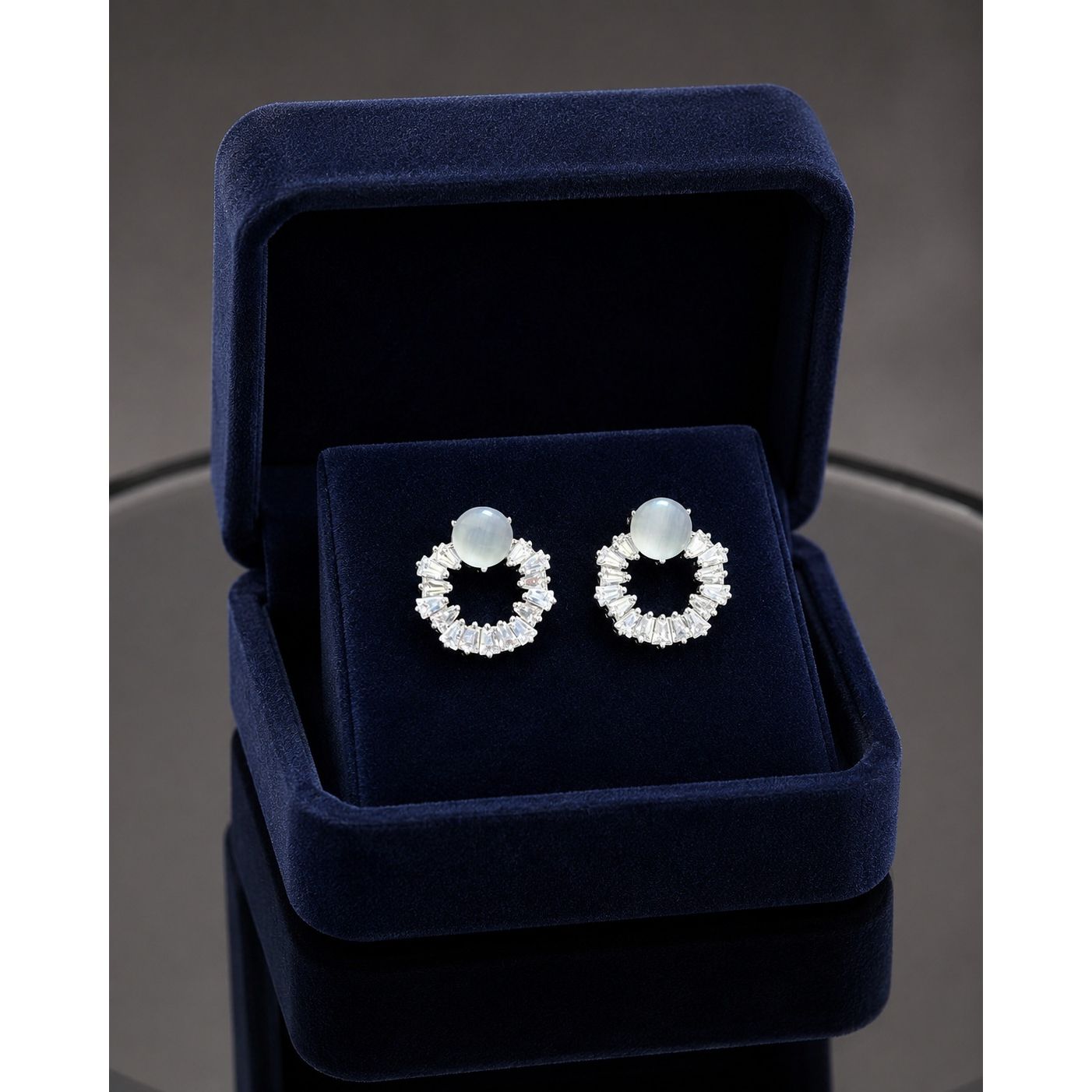 Moonstone halo crystal stud earrings displayed in a premium navy blue velvet jewelry box with sparkling baguette-cut stones and silver-tone finish.
