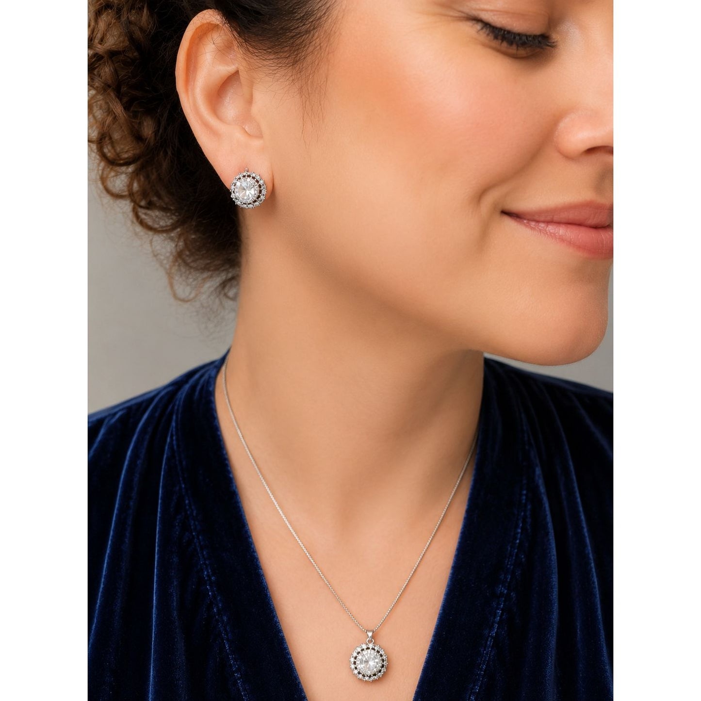Model wearing a silver halo crystal pendant necklace and matching stud earrings with brilliant round-cut stones and sparkling halo detailing.
