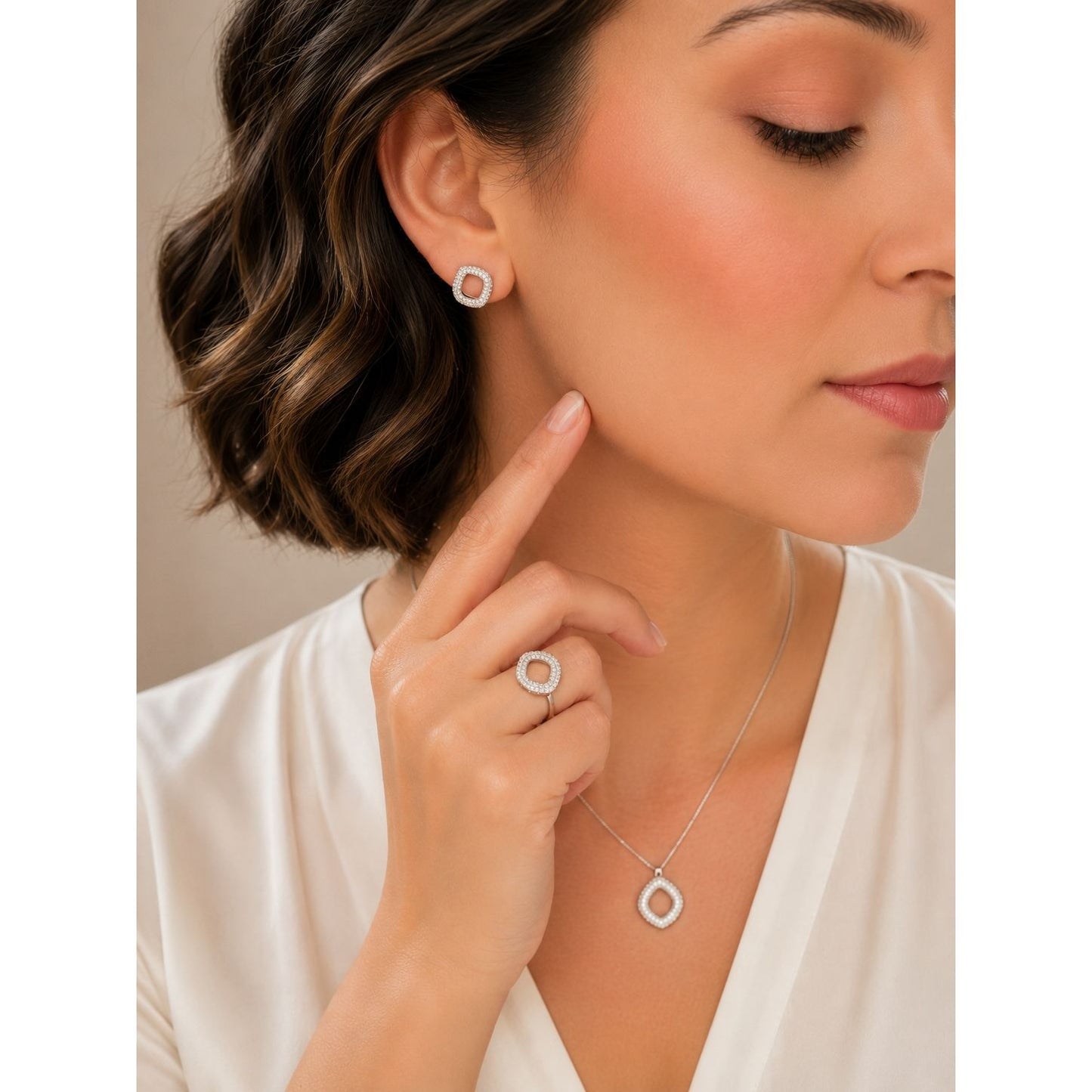 Woman wearing silver cushion-shaped crystal stud earrings, matching pendant necklace, and statement ring with sparkling pavé detailing in a modern jewelry set.