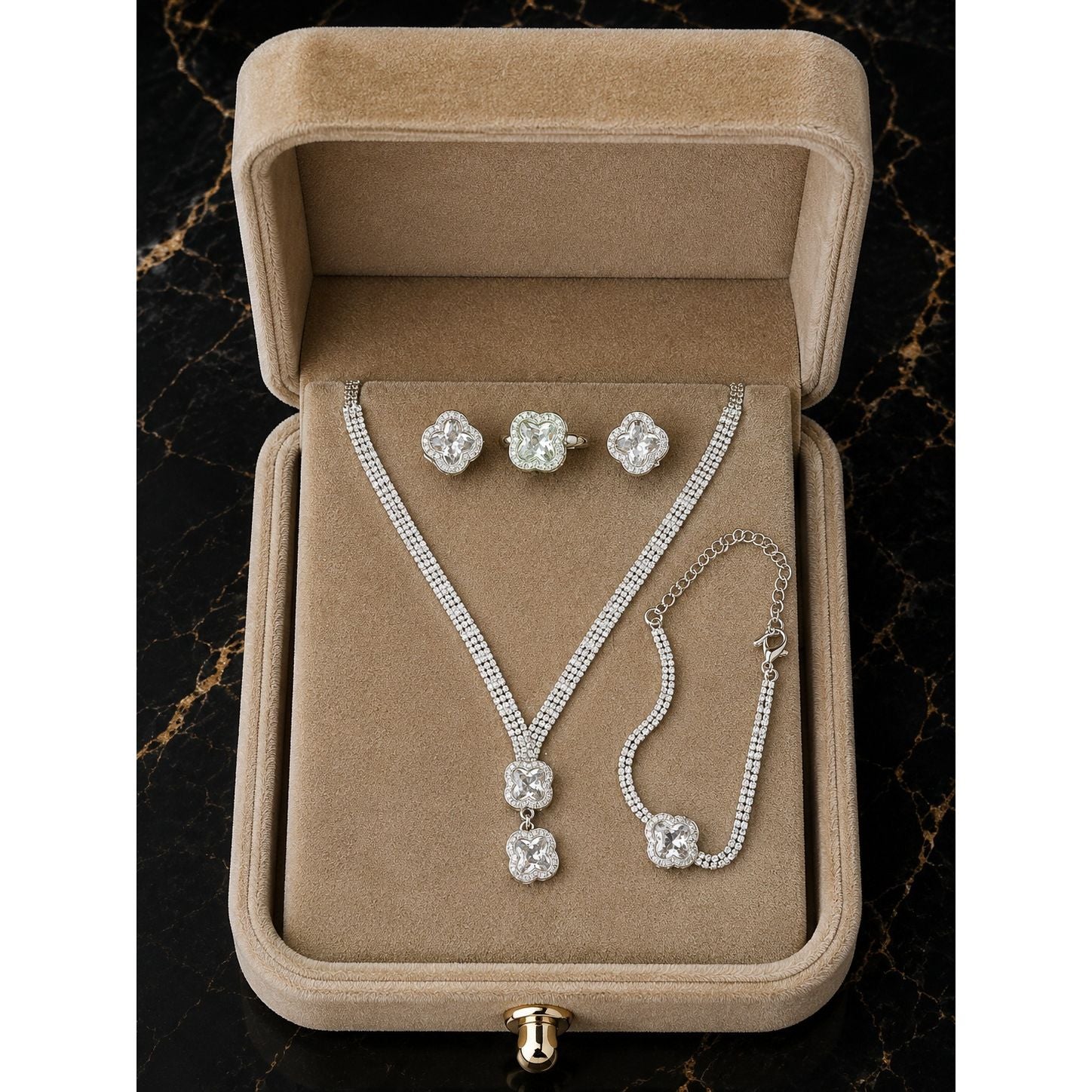 Luxury silver clover crystal jewelry set displayed in a premium champagne beige velvet jewelry box featuring a necklace, stud earrings, ring, and matching bracelet.