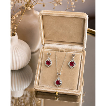 Ruby red heartdrop necklace and matching drop earrings displayed in a premium champagne velvet jewelry box with sparkling crystal detailing.